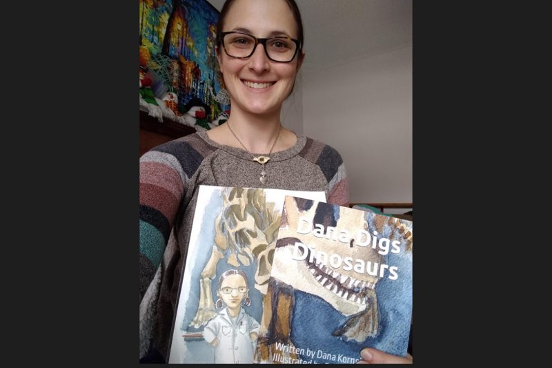 Dana Korneisel holds a copy of the first book in her children's series, "Dana Digs Dinosaurs." 