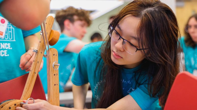 female student looks closely at catapult