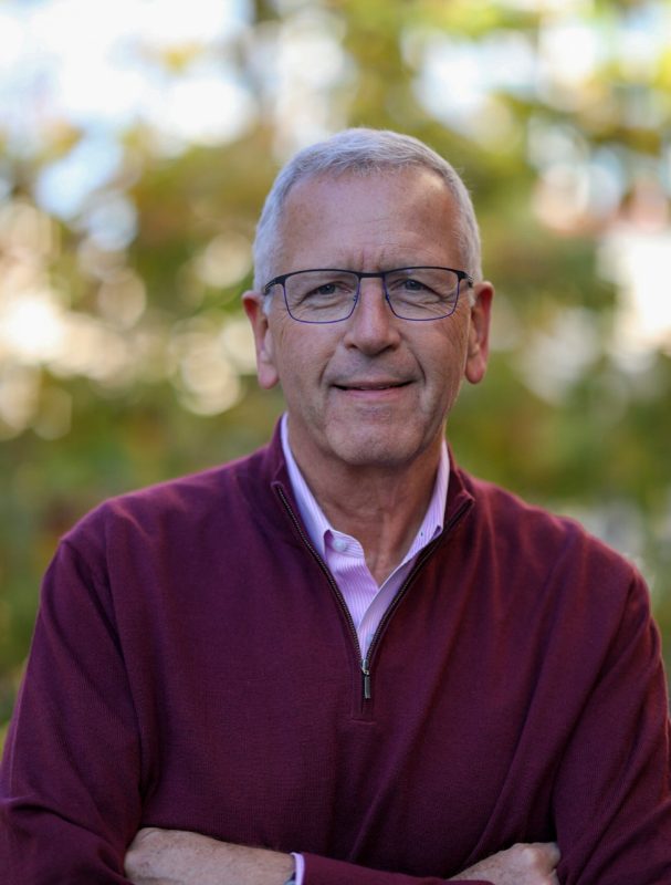 Joe DeSimone portrait of man with glasses and short gray hair with a blurred outdoor background