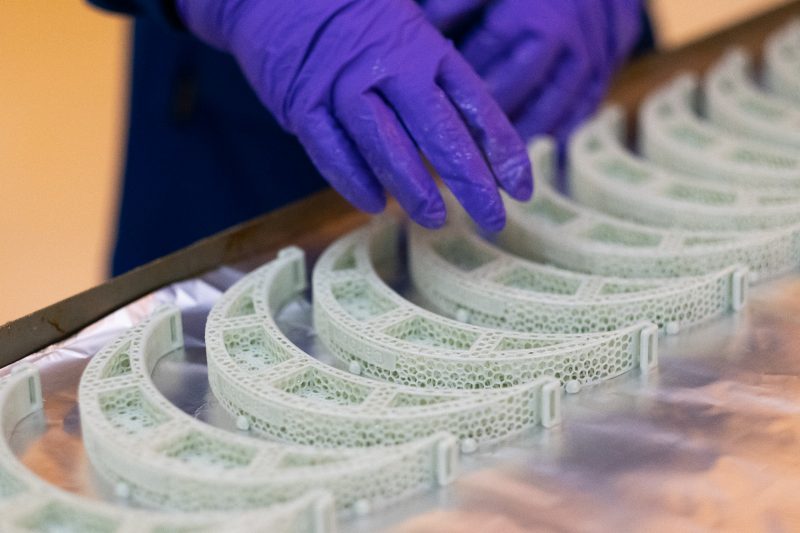face shield parts are laid out on a table. Researcher with gloved hands counts them.