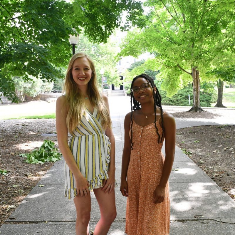 two women pose on shaded sidewalk during the summer